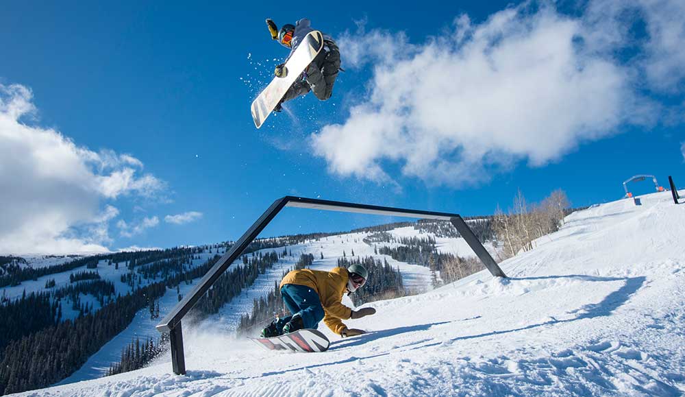 Snowboarders flying off jumps on the Snowmass mountain terrain.
