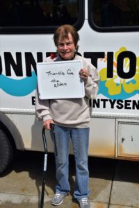 Woman holding a thank you sign outside a bus, which is part of the Senior Connection by the Limelight Ketchum Community Fund.