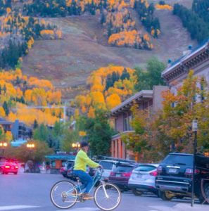 Woman riding a bike in front of a mountain with fall leaves - Offseason in Aspen, Ketchum, Snowmass
