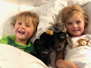 Two kids with stuffed animals in their bed at the Limelight Hotel Ketchum.